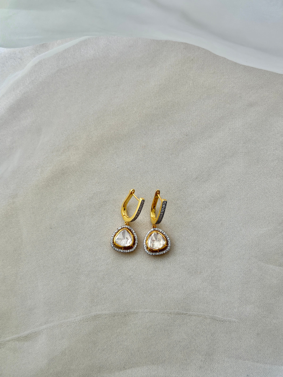 Tilak Earrings featuring clear triangular drops with sparkling stone borders suspended from gold-tone hoops.